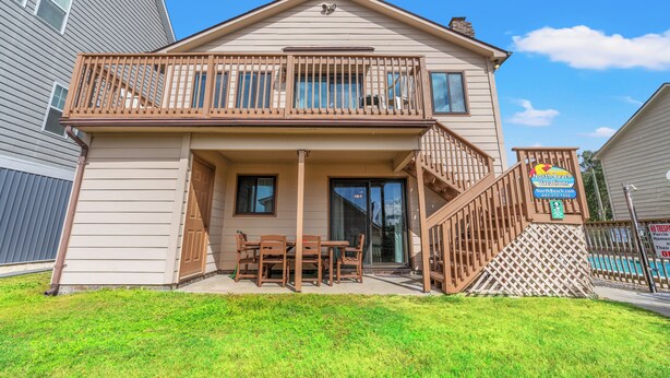 A two-story house with a balcony, a patio with a table and chairs, and a sign for North Beach Vacations. - Pet Friendly Newly Updated Home + Free Attraction Tickets! (North Myrtle Beach)