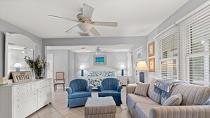 A well-lit, spacious living room with a white console, two blue armchairs, a striped sofa, and a ceiling fan.