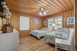 Quarto com painéis de madeira, duas camas, um ventilador de teto e quadros nas paredes.