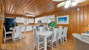 A wooden-paneled kitchen with white cabinets, a dining table with chairs, and a ceiling fan.