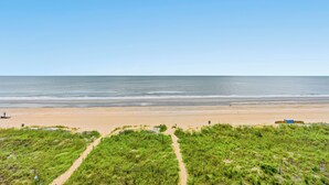 Ein Strand mit einem klaren Weg zum Wasser, einem sandigen Bereich und etwas Vegetation im Vordergrund.