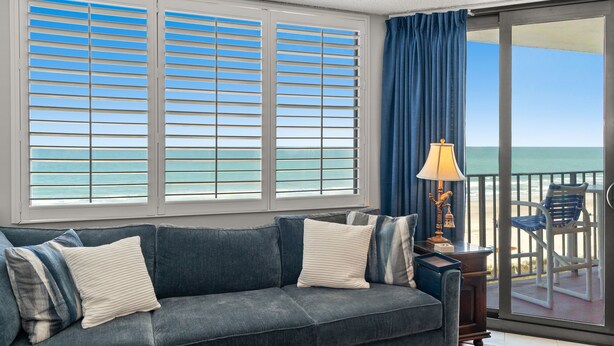 Ein Wohnzimmer mit einer Couch, Kissen, einer Lampe und Meerblick durch große Fenster.