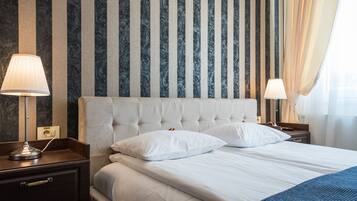 Una habitación de hotel con cabecera capitonada, ropa de cama blanca, una mesita de noche con lámpara y un enchufe.