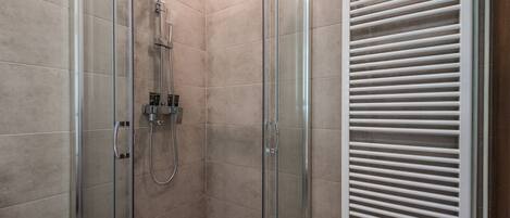 A glass-enclosed shower with a handheld showerhead and a wall-mounted control panel.