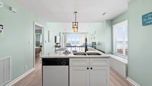 Una cocina moderna con lavavajillas, armarios blancos y una ventana con persianas.