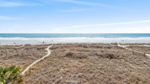 Una playa con cielo despejado, un sendero arenoso y vegetación escasa.