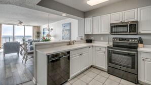 A modern kitchen with white cabinets, stainless steel appliances, and a large window overlooking the ocean. - 10th floor newly remodeled unit + Free Attraction Tickets! (North Myrtle Beach)