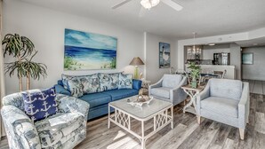 A living room with a blue sofa, patterned armchairs, a coffee table, and a ceiling fan. - 10th floor newly remodeled unit + Free Attraction Tickets! (North Myrtle Beach)
