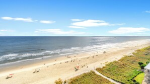 Ein Strand mit einem Pfad, der zu einem Gebäude mit einem Balkon führt.