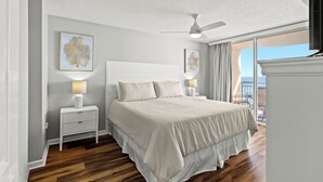 Ein Schlafzimmer mit einem großen Bett, zwei Nachttischen inklusive Lampen, einem Deckenventilator und Blick ins Freie.