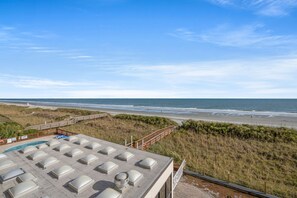 A beach view from a building with a pool and a wooden deck leading to the beach.