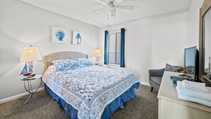 A bedroom with a bed, two bedside lamps, a ceiling fan, a desk with a computer, and a mirror. - Nicely decorated unit with Indoor/Outdoor pools + Free Attraction Tickets! (North Myrtle Beach)