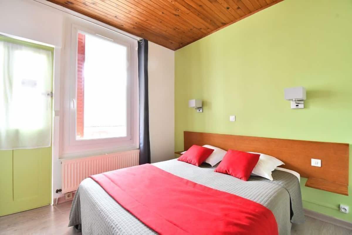 A room with a bed, a window, a radiator, and a wooden ceiling.