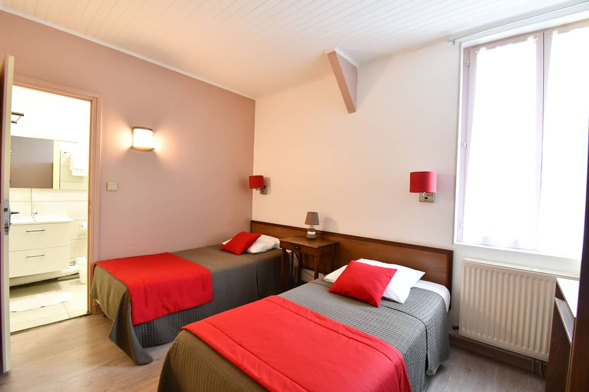 A hotel room with two beds, a bathroom, a window, and a radiator.