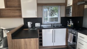 Una cocina funcional con encimera negra, armarios blancos, horno integrado y ventana con persianas.