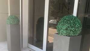 A modern entrance with a glass door, two potted plants, and a doormat with "IN" on it. - JN Boutique Hotel (Bucharest)