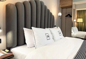 Una habitación de hotel moderna con una cama grande, ropa de cama blanca y un diseño de cabecera único.
