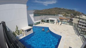 En pool på taket med kristallklart blått vatten, omgiven av modern arkitektur och med utsikt över en sluttning.