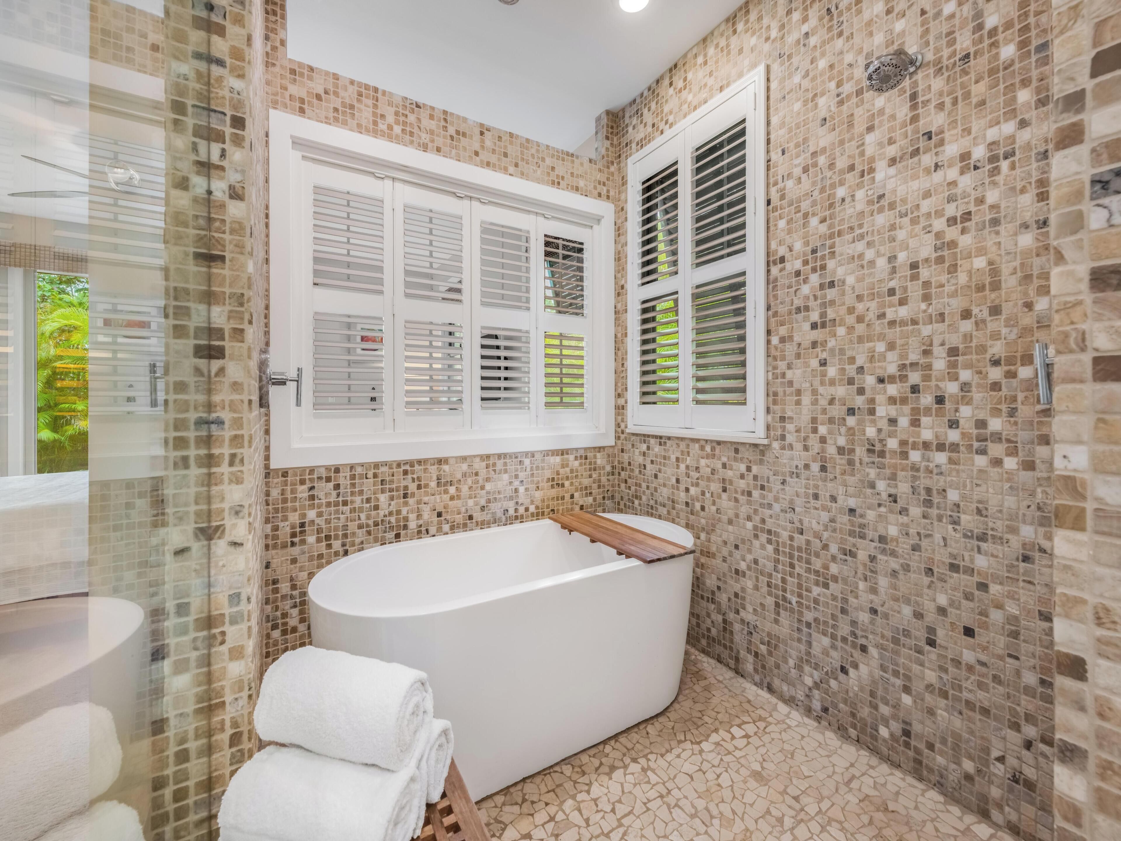 A bathroom with a freestanding bathtub, tiled walls, and a window with shutters.