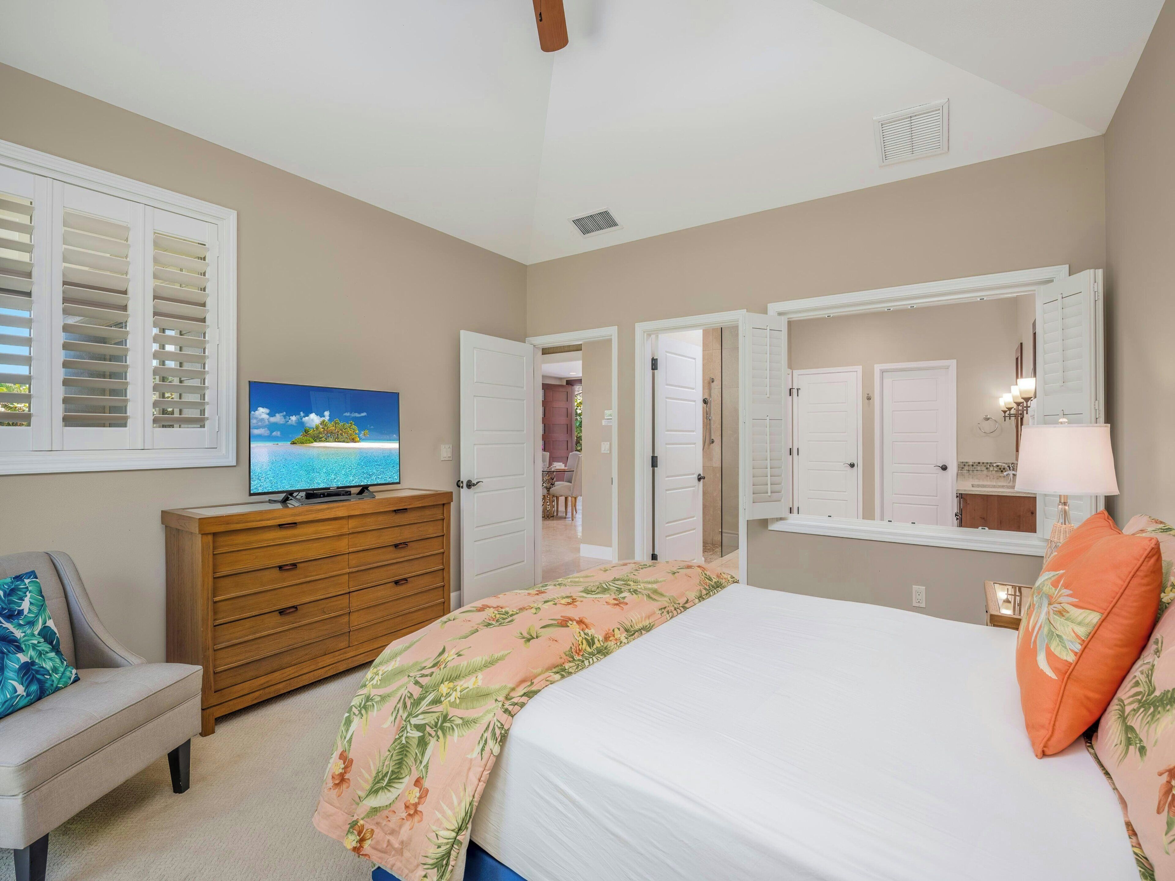 A bedroom with a bed, a TV, a dresser, and a door leading to another room.