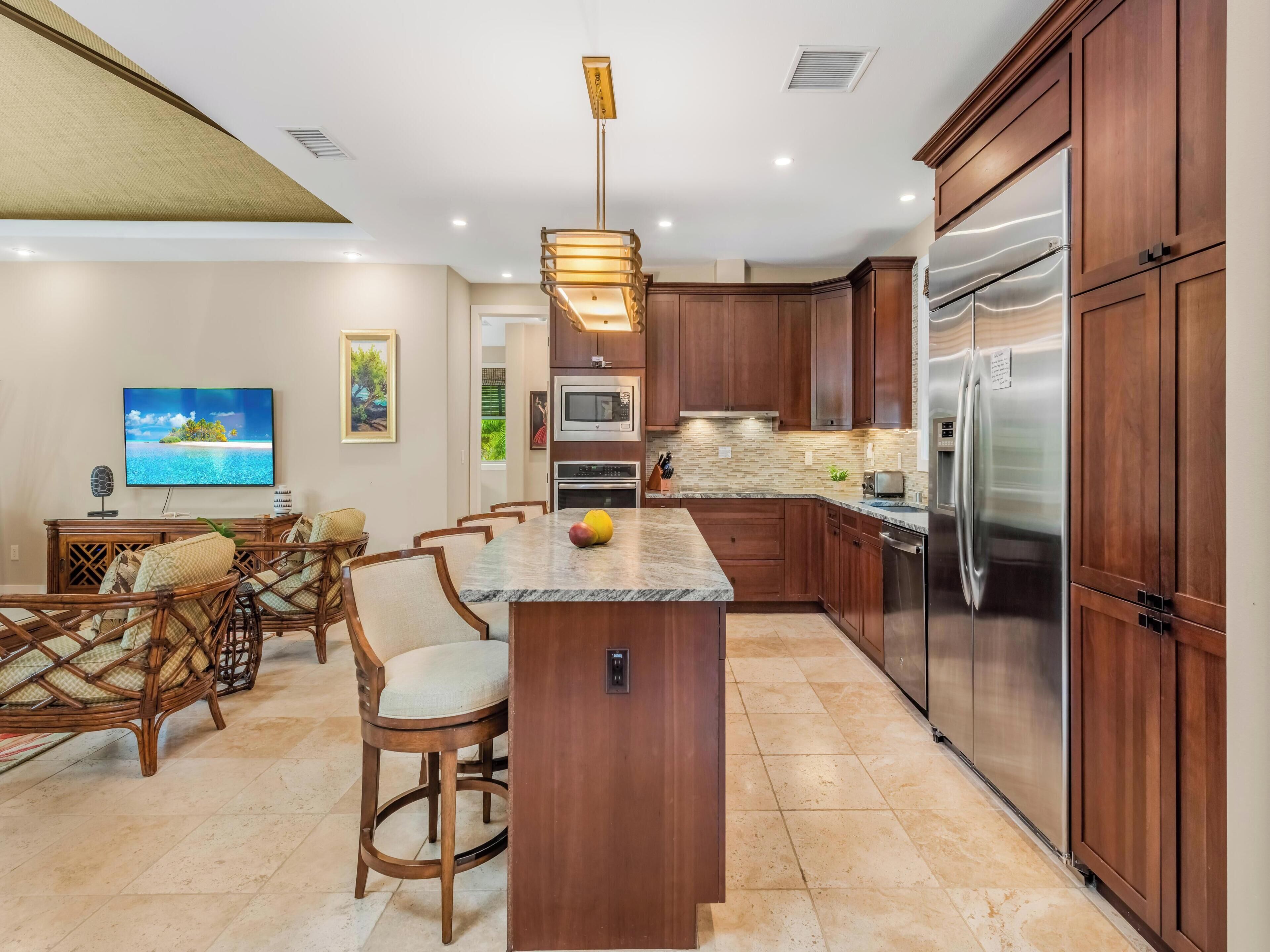 A modern kitchen with wooden cabinets, a stainless steel refrigerator, a built-in oven, and a large island with seating.