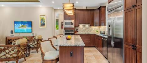 A modern kitchen with wooden cabinets, a stainless steel refrigerator, a built-in oven, and a large island with seating.