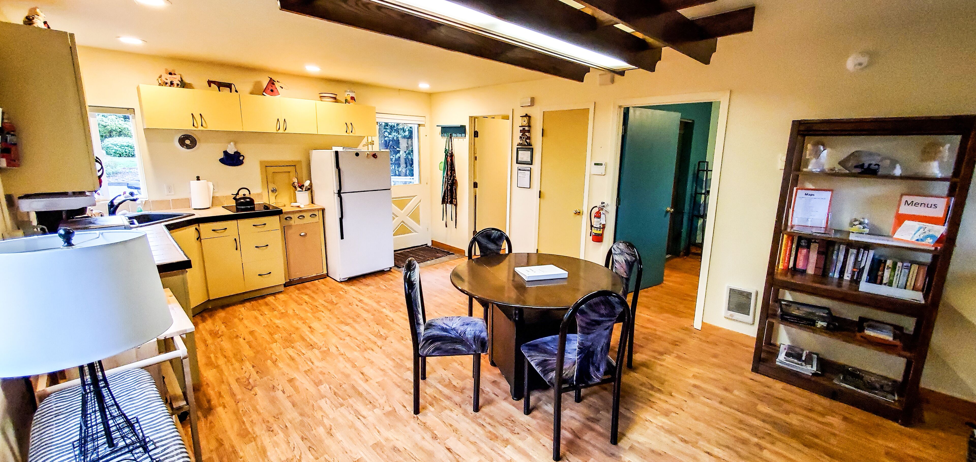 Una cocina compacta con piso de madera, una mesa de comedor con sillas, una estantería y un refrigerador.