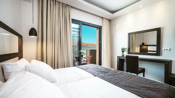 A modern hotel room with a large bed, a desk, a chair, and a view through a glass door. - Abaton Luxury Resort (Zakynthos)