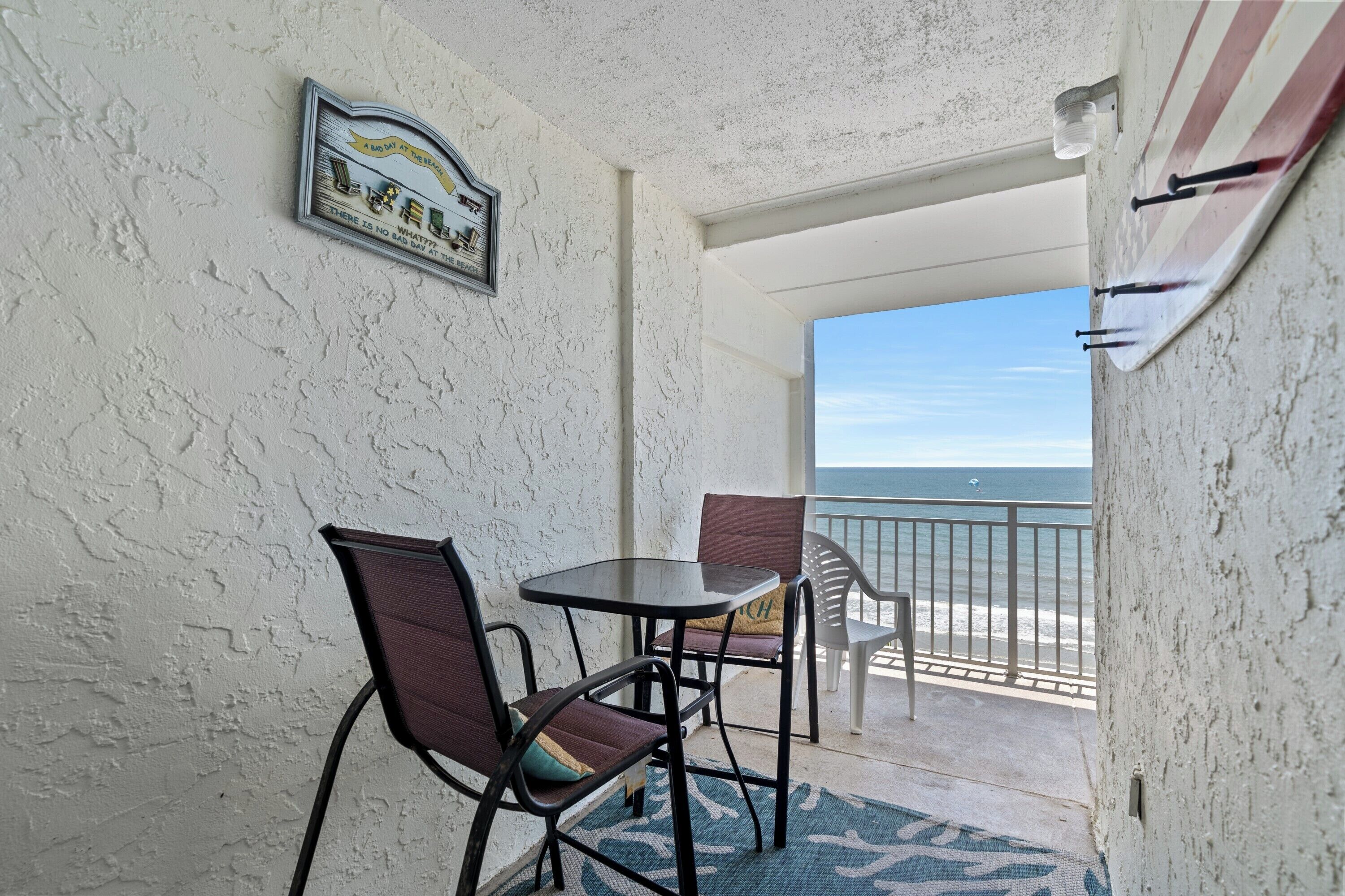 A balcony with a table and chairs, a view of the ocean, and a sign on the wall.