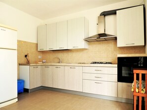 A kitchen with light-colored cabinets, a gas stove, a sink, and a blue trash bin.