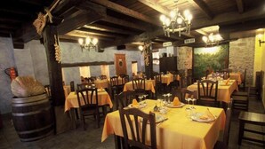A restaurant with multiple tables set for dining, wooden chairs, and a rustic interior with stone walls and wooden beams. - Casa Rural Bentazar (Legutiano)
