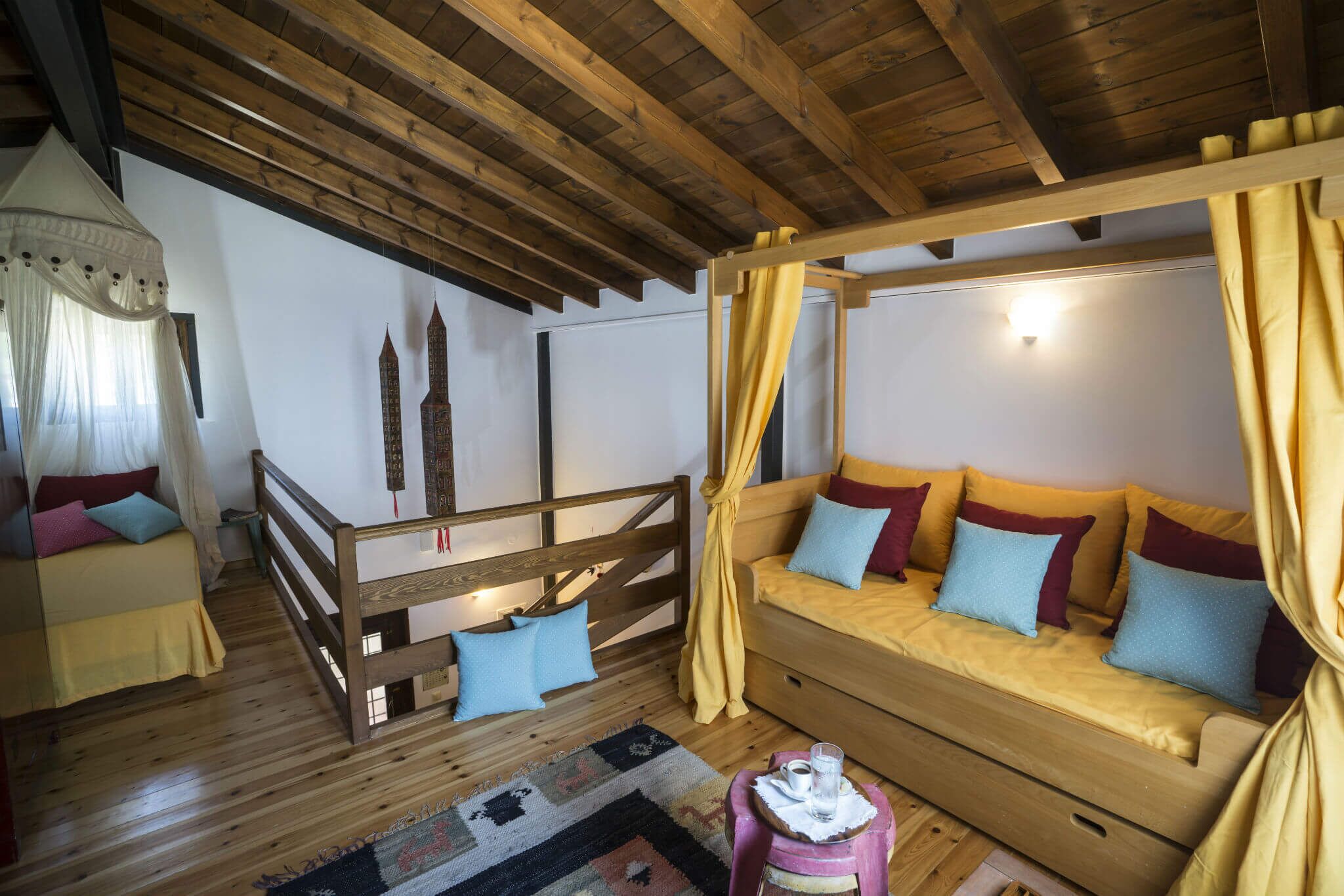 A cozy room with a wooden ceiling, a bed with a canopy, a sofa with cushions, and a small table with a glass and a cup.