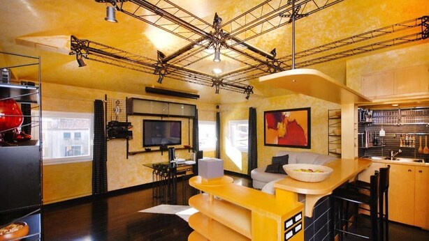 Una cocina moderna con encimera amarilla, un área de comedor con sofá y un televisor montado en la pared.