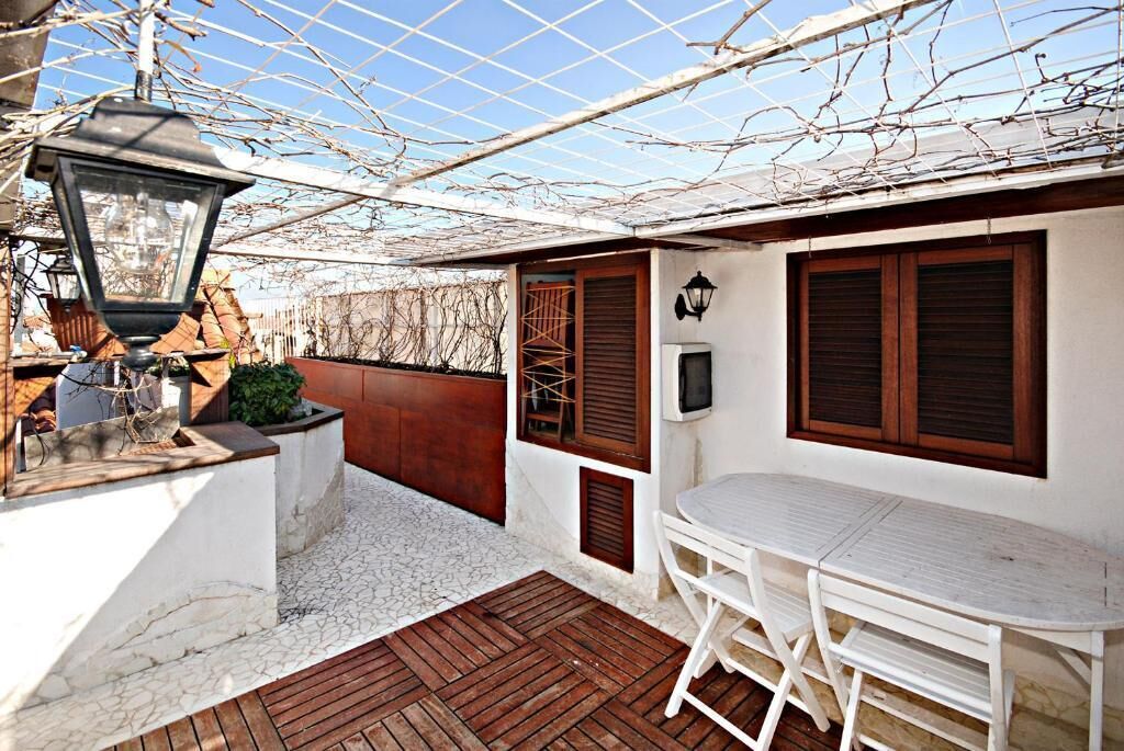 A covered outdoor seating area with a table and chairs, a lantern, and a wall-mounted TV.