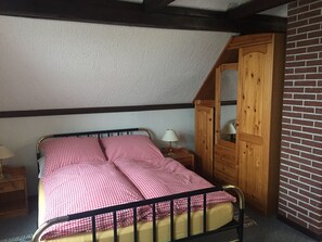 Un dormitorio con estructura de cama metálica, ropa de cama a cuadros, un armario de madera y una mesita de noche con lámpara.