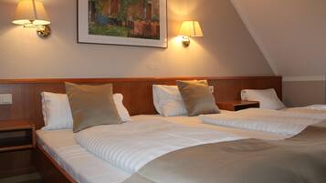 A hotel room with two beds, each with a wooden headboard, white bedding, and two bedside lamps. There is a framed painting on the wall above the beds.