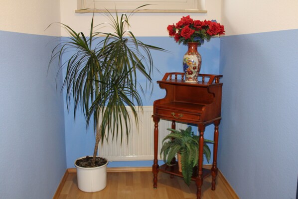 A corner with a potted plant, a wooden side table with a vase of red flowers, and a radiator.