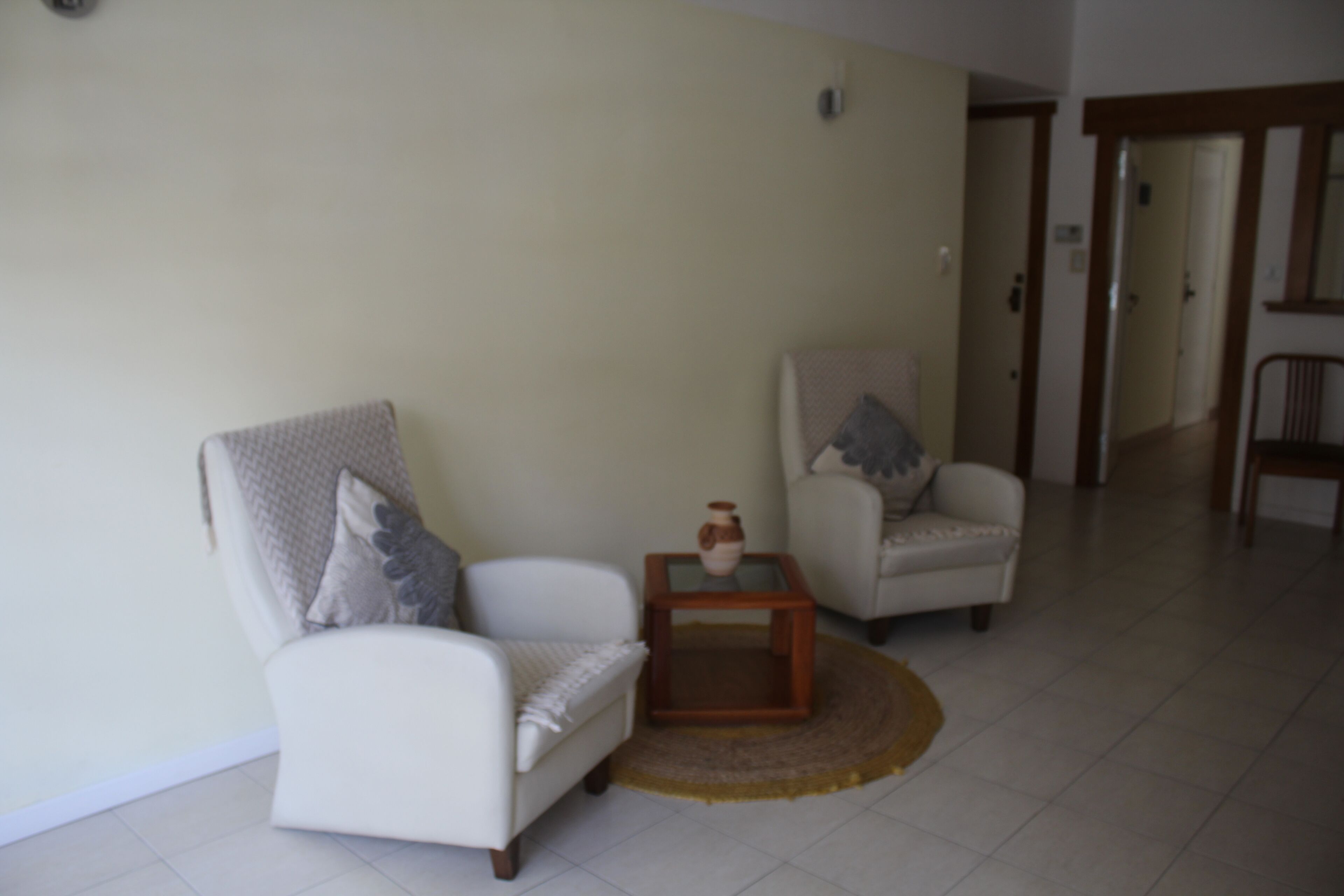 Een woonkamer met twee witte fauteuils, een klein houten bijzettafeltje en een beigekleurig vloerkleed.