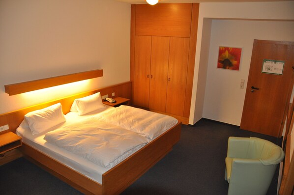 A hotel room with a wooden bed, a nightstand, a chair, and a wardrobe. - Hotel Lamm (Neckarsulm)