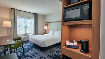 A hotel room with a bed, a desk with a chair, a microwave, a coffee maker, and a window with curtains.