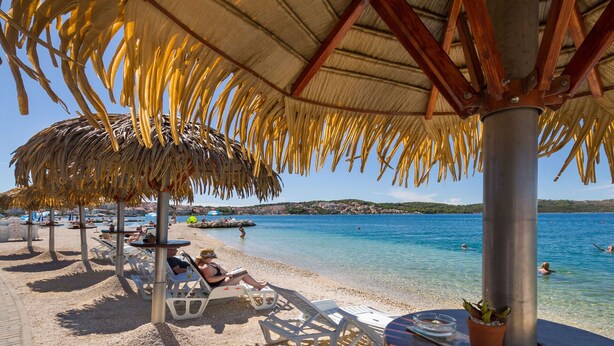 A beachside area with thatched umbrellas, lounge chairs, and a clear view of the sea. - House Diamond, Okrug Gornji - ideal for relaxing holidays for families & friends (Okrug Gornji)