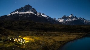 A mountainous landscape with a small settlement featuring illuminated buildings near a body of water. - Refugio Vértice Paine Grande Hostel (Torres del Paine)
