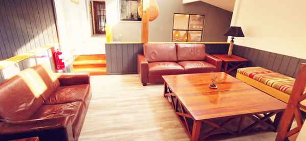 A cozy living room with a wooden coffee table, leather sofas, and a small side table. - Refugio Vértice Paine Grande Hostel (Torres del Paine)
