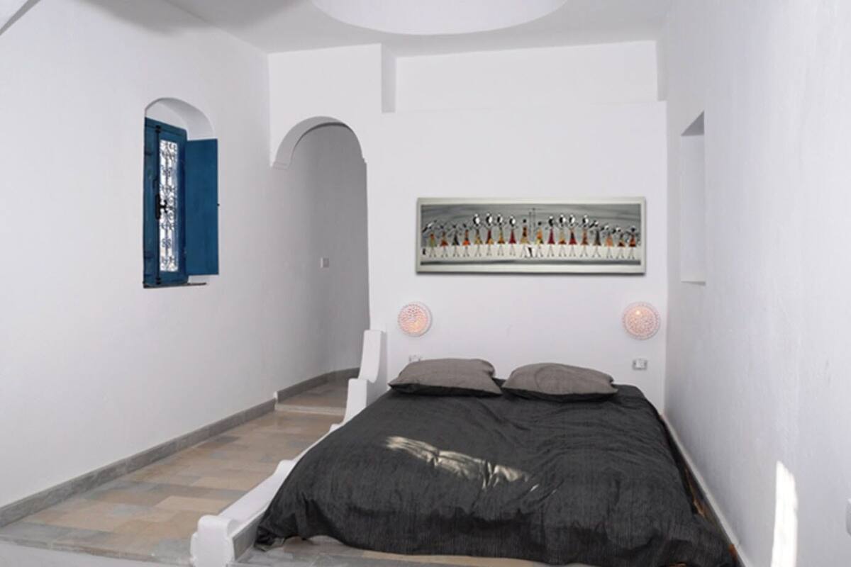 Une chambre à coucher avec un lit, une porte bleue et une œuvre d’art accrochée au mur.