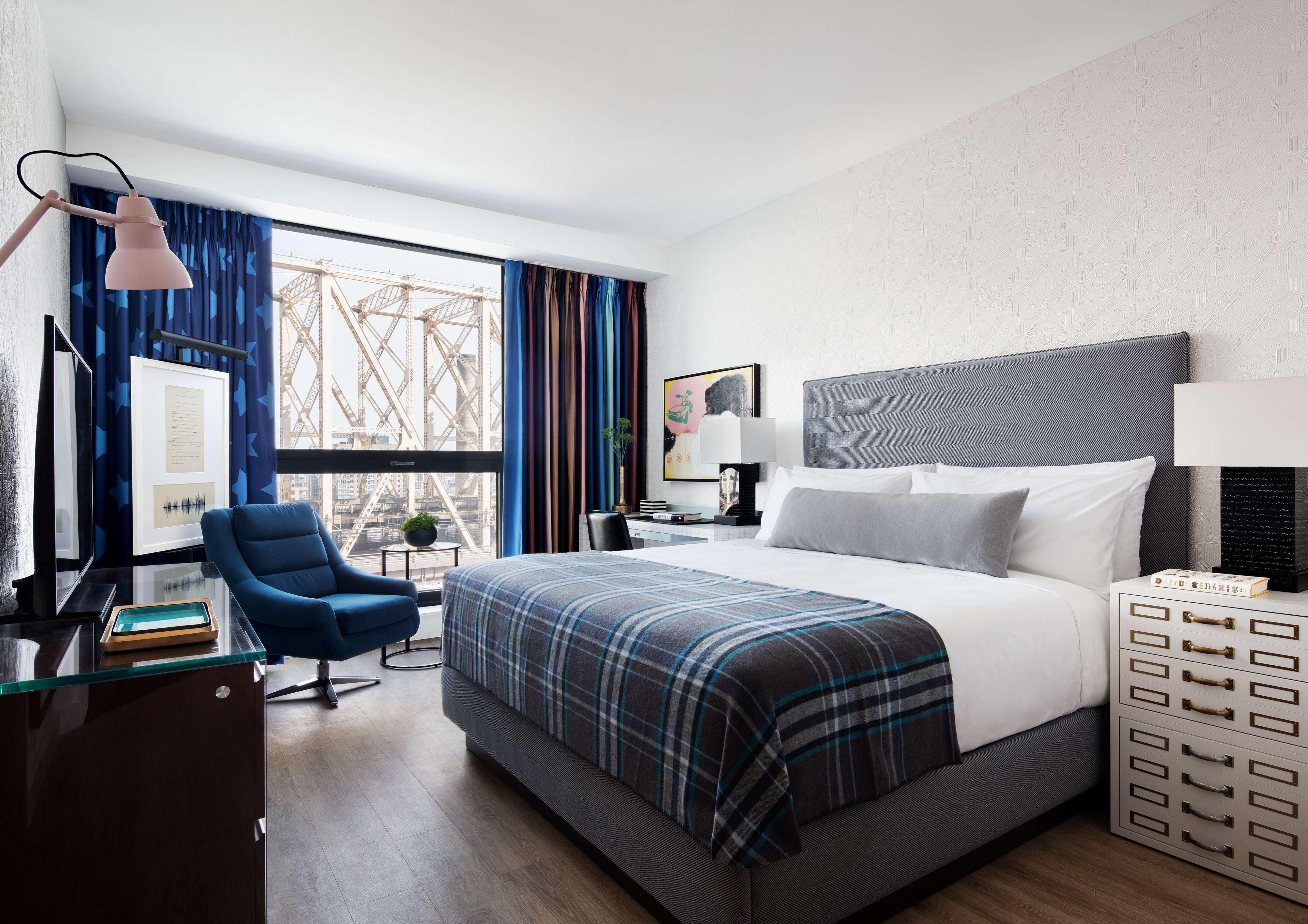 Habitación de hotel con una cama grande, un escritorio con lámpara, una silla y vistas a un puente.