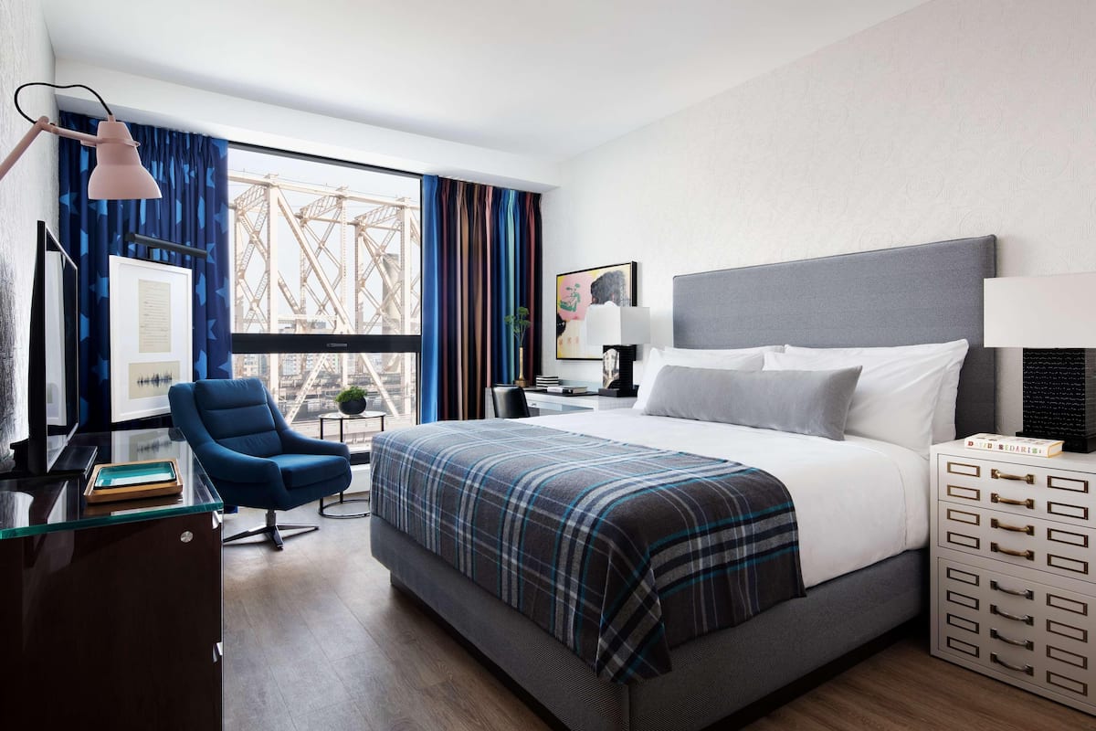 A hotel room with a large bed, a desk with a lamp, a chair, and a view of a bridge.