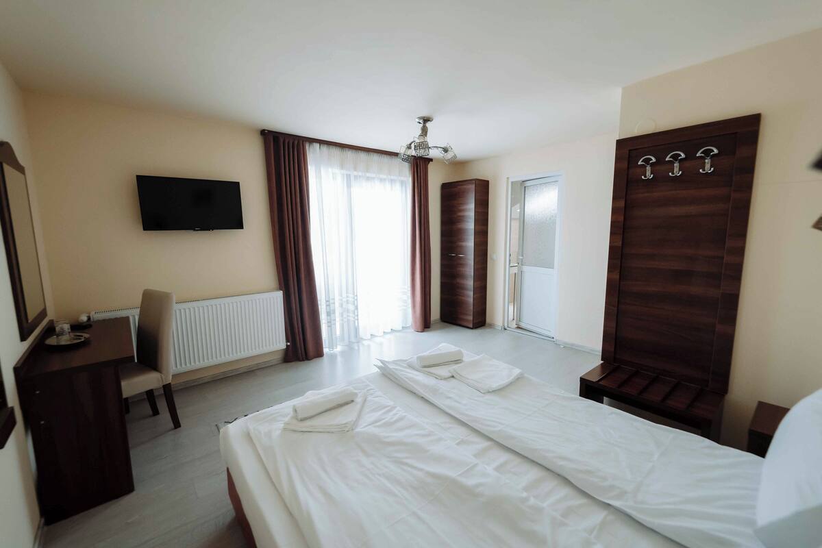 A hotel room with a bed, a desk, a chair, a television, and a wardrobe.