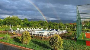 A pool area with lounge chairs and a netted tennis court. - Popasul Montan (Avrig)