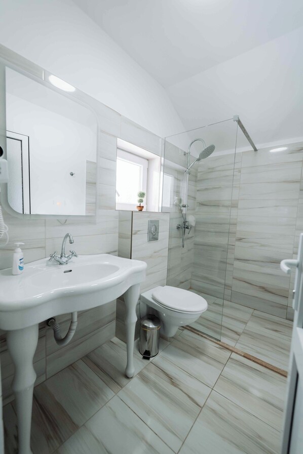 A modern bathroom with a white sink, toilet, and glass-enclosed shower. - Popasul Montan (Avrig)