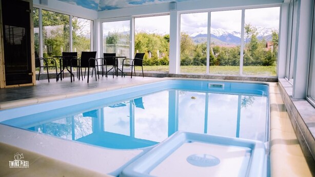 A swimming pool with a view of mountains and greenery, surrounded by large windows and a ceiling with a sky design. - Popasul Montan (Avrig)